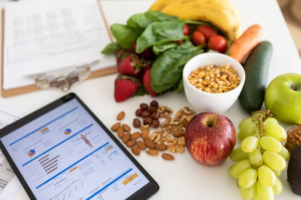 Fresh fruit and vegetables beside a tablet showing health test results